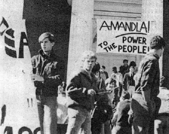 A picture of a Colby protest in the 1980s. A crowd of students stand around Miller steps. A banner hangs on the columns of Miller, which reads: 'Amandla! Power to the people!'.